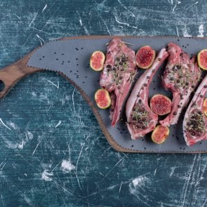 Raw rib chops in wooden board with figs and dried herbs. High quality photo